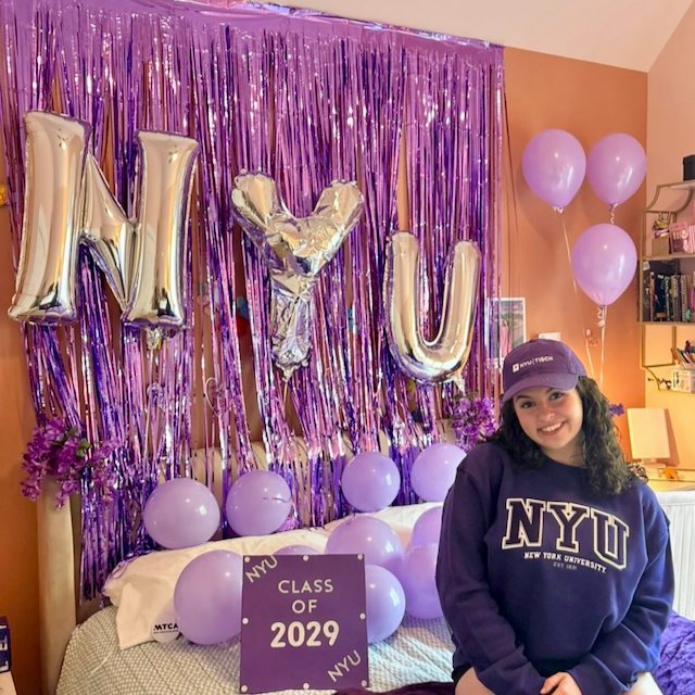  Eva Hurley wearing an NYU hat, sweatshirt sits around NYT balloons and purple streamers